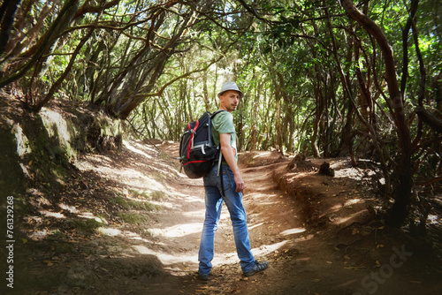 Man wearing a backpack stands amidst the trees in a dense forest. Tenerife, Spain