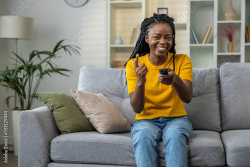 Young woman in yellow tshirt sitting on the sofa and looking excited