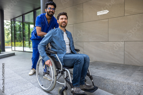 Young dark-haired male nurse taking a patient in wheelchair for walk