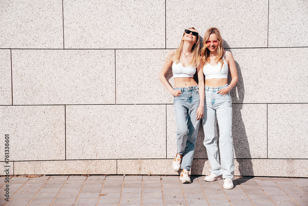 Two young beautiful smiling hipster female in trendy summer white top and jeans clothes. Carefree women posing in the street. Positive models having fun outdoors. Cheerful and happy. In sunglasses Two young beautiful smiling hipster female in trendy summer white top and jeans clothes. Carefree women posing in the street. Positive models having fun outdoors. Cheerful and happy. In sunglasses