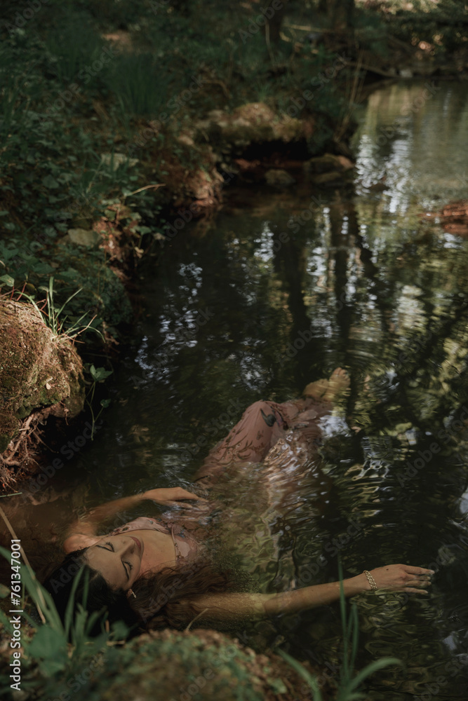 Woman floating in the river water while she dreams. Concept of spiritual connection with the natural environment and ethereal atmosphere between two worlds. Woman floating in the river water while she dreams. Concept of spiritual connection with the natural environment and ethereal atmosphere between two worlds.