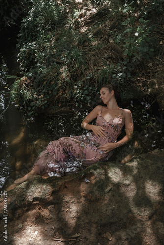 Young woman lying on the river bank while she sleeps and rests meditating. Concept of spiritual connection with the natural environment and ethereal atmosphere between two worlds.