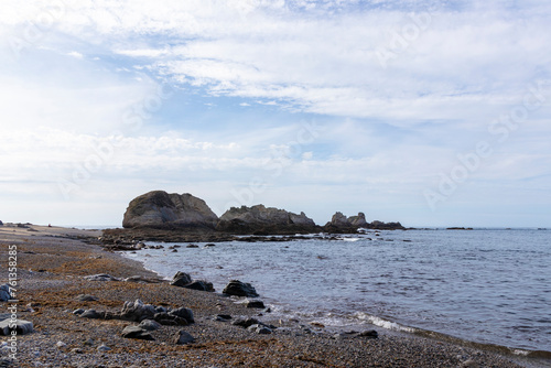 A serene beach with large rocks in the water, a pebbly shore, under a sky with wispy clouds, evoking tranquility