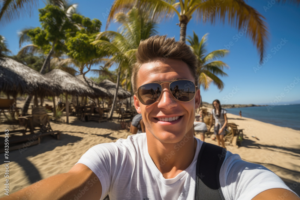 Man wearing sunglasses and white shirt is smiling at camera on beach