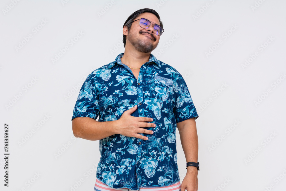 A content middle-aged man wearing a Hawaiian shirt rubs his belly, indicating a feeling of fullness, against a white background. A content middle-aged man wearing a Hawaiian shirt rubs his belly, indicating a feeling of fullness, against a white background.