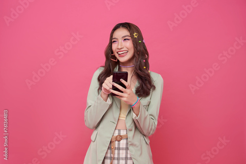 Young smiling happy asian woman 20s using mobile cell phone isolated on pink background. portrait People lifestyle concept