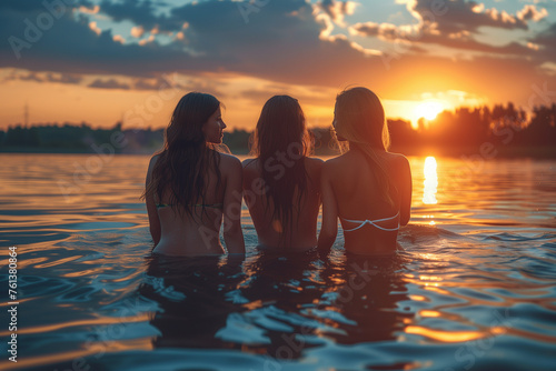Three women are sitting in the water, enjoying the sunset