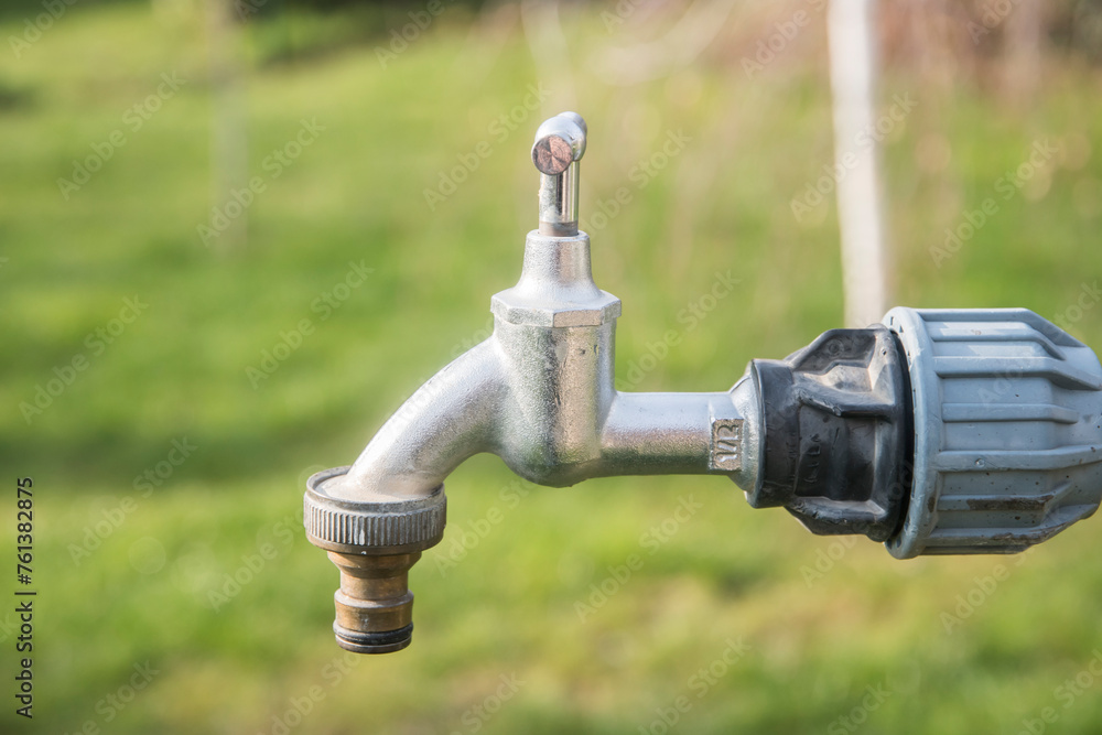 Water tap with metal garden hose adapter closeup on green grass background