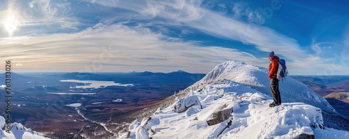man with backpack stands on snowy summit of Katahdin, Maine in winter