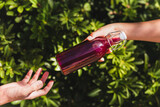 Woman's hand giving a glass bottle of nutritious juice drink with plant leaf background.