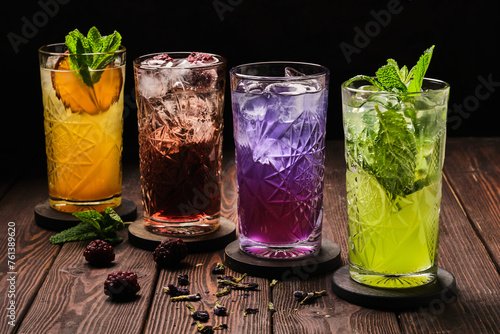 A variety of refreshing cocktails in different colors, garnished with fresh mint leaves, served on a rustic wooden table.