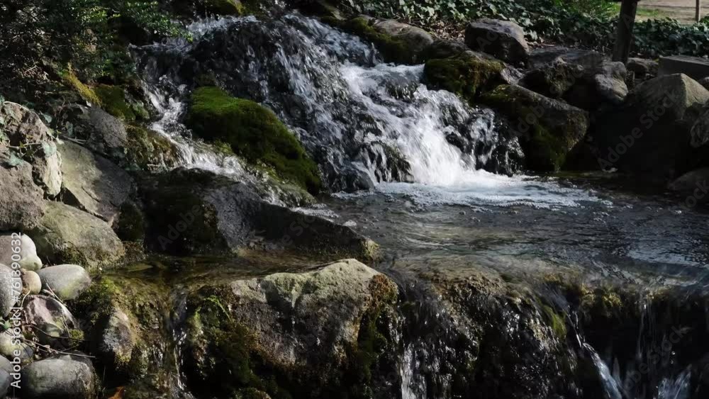 A small waterfall flows over rocks with green moss in the botanical garden in the center of Belgrade, Serbia. Horizontal slow motion footage. Details of nature in a quiet rainforest A small waterfall flows over rocks with green moss in the botanical garden in the center of Belgrade, Serbia. Horizontal slow motion footage. Details of nature in a quiet rainforest