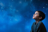 A contemplative kid model lost in thought, against a solid wall of blue background, contemplating the mysteries of the universe with wonder.