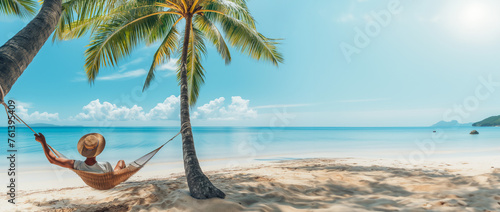 Man relaxes on a hammock between palm trees with the turquoise sea and blue summer sky. Beach relaxation. Tropical paradise. Panoramic banner with copyspace