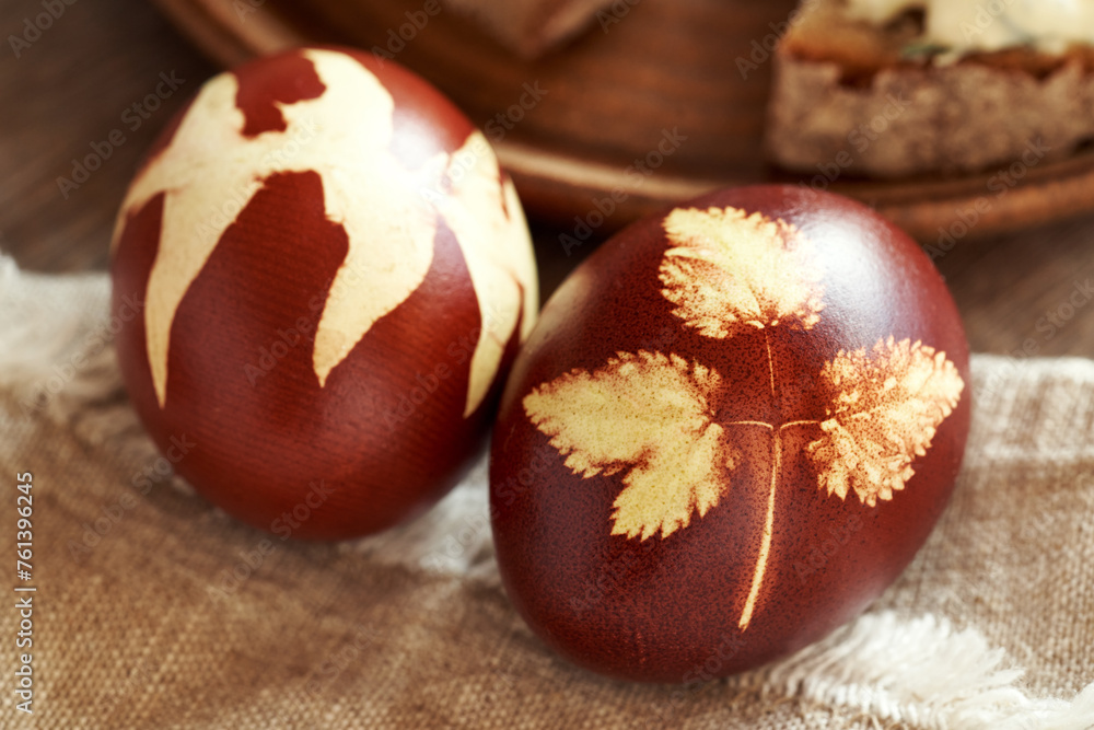 Close up of a brown Easter egg dyed with onion peels with a pattern of fresh leaves - obrazy, fototapety, plakaty 