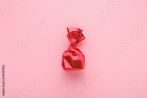 Candy wrapped in bright red foil paper on light pink table background. Pastel color. Closeup. Top down view.