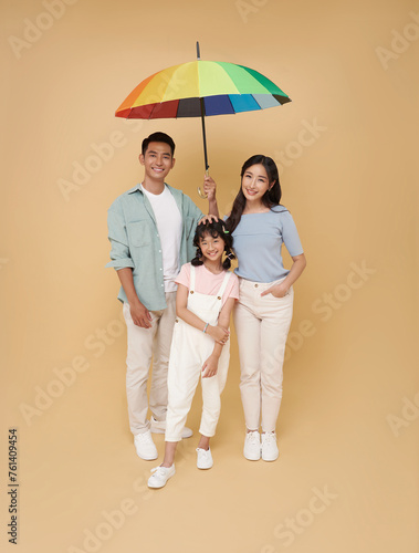 Happy asian family under big colorful umbrella isolated on nude color background. Family Protection and Life and health insurance.