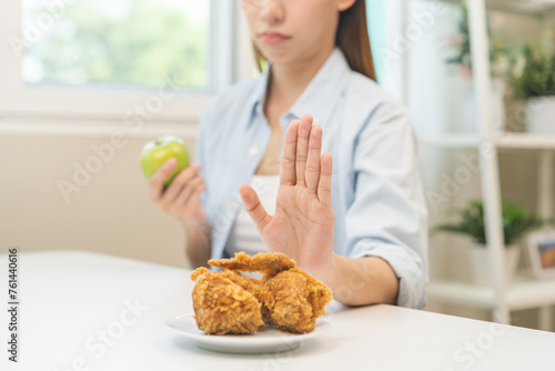 Diet, Dieting asian young woman hand push out, reject fried chicken on plate, deny to eat fast, junk food choose green apple or fruit, girl eat low fat for good healthy, getting weight loss people. photo