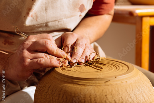 Crop artisan using ribbon tool on clay pot photo