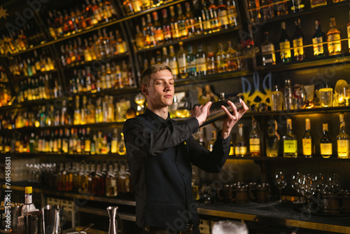 Skilled bartender prepares cocktail in metal shaker in popular nightclub. Ukrainian barkeeper makes beverage for guest in restaurant