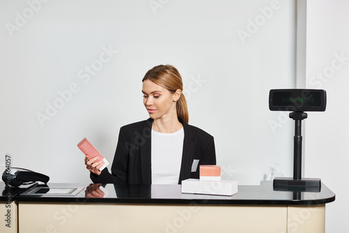 good looking shop assistant in sophisticated black blazer sitting at counter and looking at perfumes