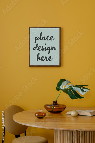 Cozy composition of dinning room interior with mock up poster frame, patterned killim rug, round table, books, cup, plants in flowerpot, orange lamp and personal accessories. Home decor. Template. photo