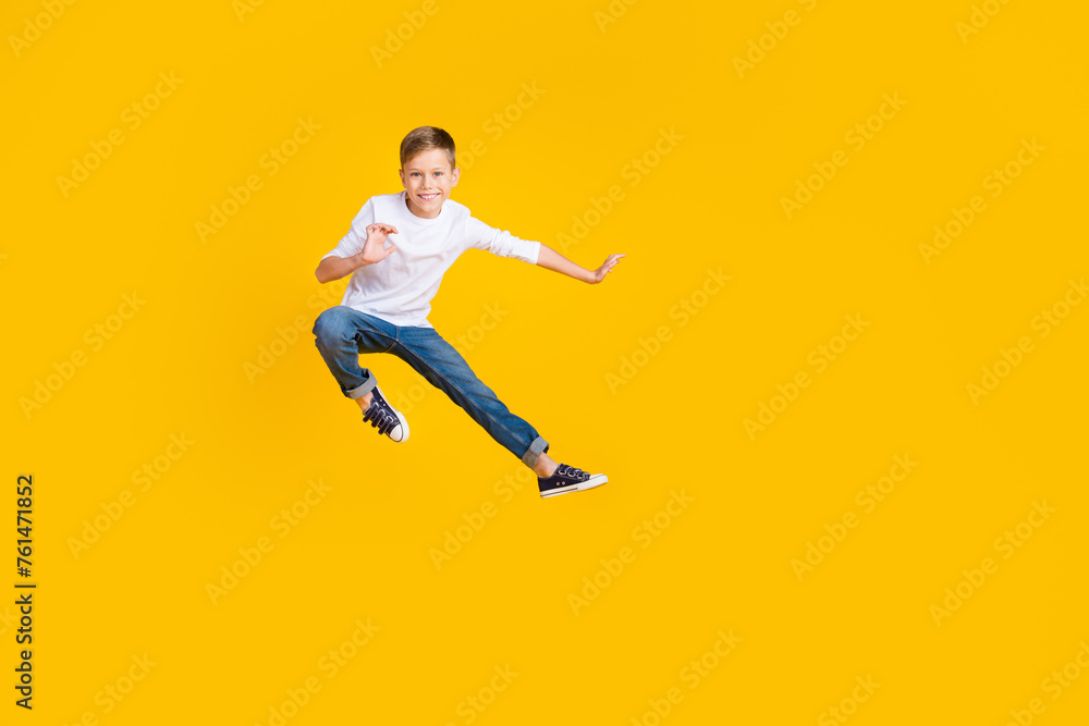 Full length photo of funky positive kid dressed white shirt practicing karate jumping high empty space isolated yellow color background