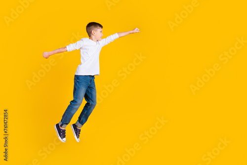Full length photo of good mood excited kid dressed white shirt jumping rising fist flying empty space isolated yellow color background