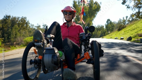 Closeup low angle of elderly senior woman riding recumbent tricycle e-bike on a path on a sunny day in a park.