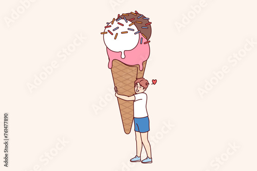 Happy boy with giant size ice cream, waffle cup and colorful sprinkles. Cheerful child hugs sweet ice cream, rejoices at opportunity to try delicious dessert in hot summer weather.