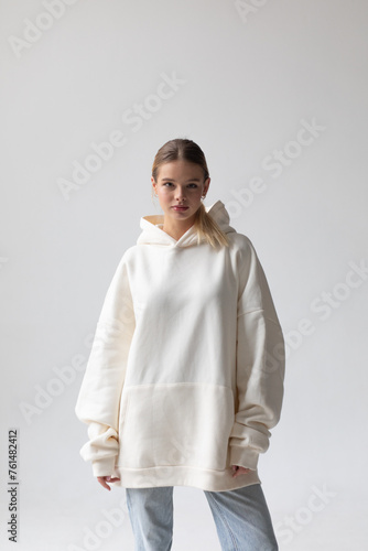 Fotografía Beautiful blonde woman in a white hoodie and blue jeans posing on a white backgr