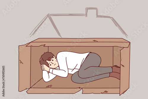 Homeless man sleeps in box on street after being fired from job due to labor market crisis. Homeless guy needs help from charity or shelter to solve temporary difficulties that cause poverty