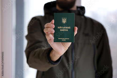 Young ukrainian conscript soldier shows his military token or army ID ticket indoors close up photo