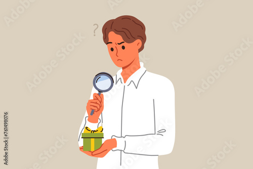 Business man examines suspiciously small gift box, using magnifying glass to spot catch. Official guy received gift as bribe for lobbying interests of company or unfair competition