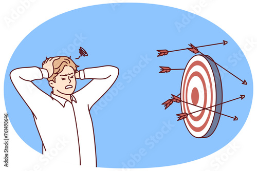 Discouraged man clutching head standing near darts board after failed attempts to hit target. Concept problems in business due to inability to complete task or KPI. Flat vector illustration
