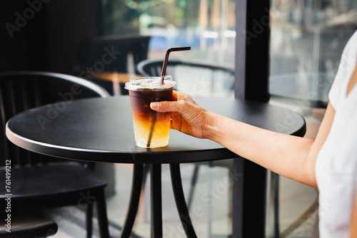 Woman drinking iced coffee in takeaway plastic cup at table outdoor cafe. photo