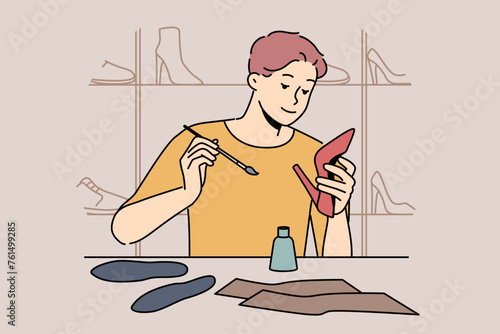 Man shoemaker holding women shoes sitting at table, repairing or making handmade footwear. Professional male shoemaker makes wardrobe items from genuine leather, located in workshop