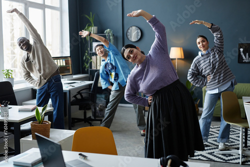 Multiethnic group of people enjoying stretching exercises starting workday in office together