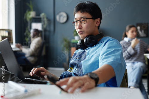 Portrait of creative Asian man with headphones using laptop at office workplace copy space