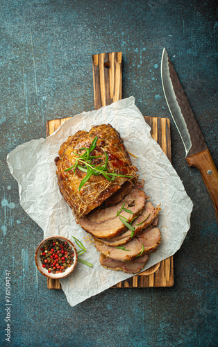 Rolled turkey roasted with spices and herbs on baking paper with knife and rustic concrete background top view. Baked cut for slices turkey fillet roll for dinner.