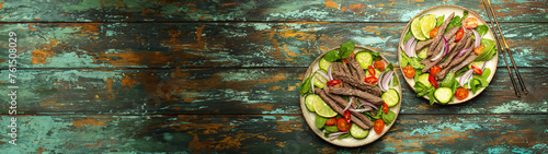 Two plates with traditional Thai beef salad with vegetables and mint top view served on rustic wooden background, healthy exotic asian meal.