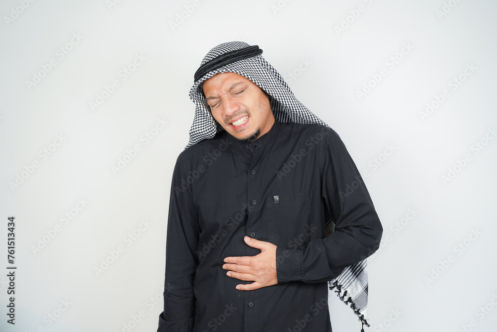 Muslim man wearing Arab turban sorban having stomach ache, bending over, holding hands on stomach, stomach cramps, gastric pain Muslim man wearing Arab turban sorban having stomach ache, bending over, holding hands on stomach, stomach cramps, gastric pain