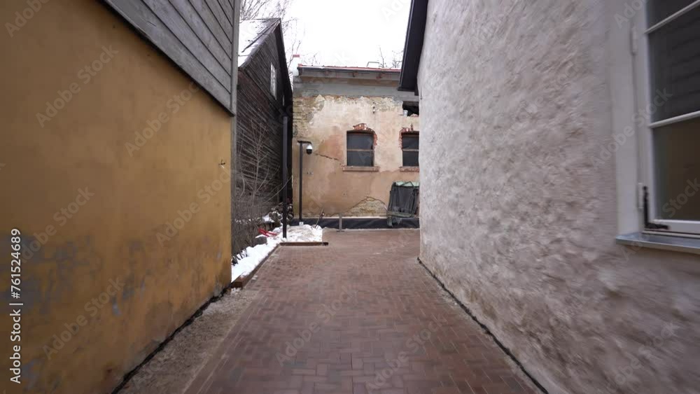 shows a narrow alley with brick pavement between an old yellow building and a white modern building with metal gate shows a narrow alley with brick pavement between an old yellow building and a white modern building with metal gate