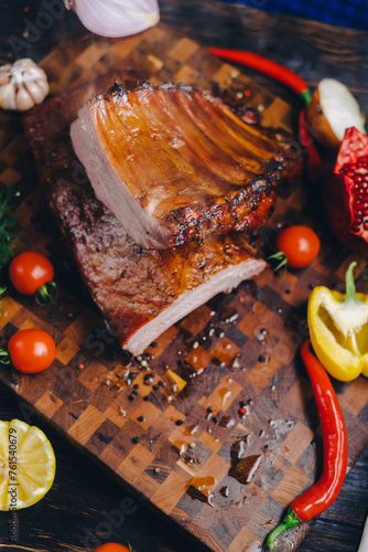 roasted pork ribs in a smokehouse, standing on a cutting board, garnished with rosemary, pepper, chili pepper, tomato, lemon, pomegranate. aromatic baked meat