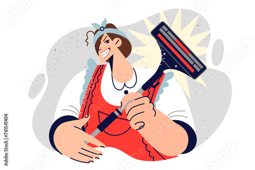Woman housewife holds vacuum cleaner and smiles slyly, dressed in apron for housework