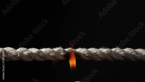 Rope stretched tight and slowly burning apart, finally snapping in two. Concept of dangerous stress or stressful situation like divorce separation, deadlines, failure, or tension. photo