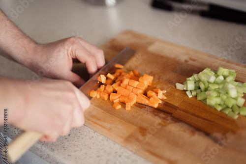 A detailed shot of hands cutting fresh carrots and celery on a wooden board.
