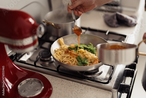 Pouring sauce over pasta in a pan, home cooking concept, kitchen setting