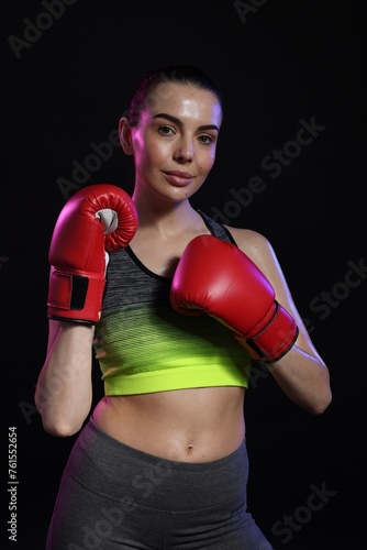 Portrait of beautiful woman wearing boxing gloves in color lights on black background