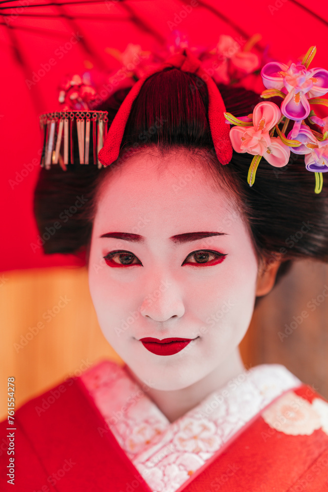 A geisha’s face is perfectly framed by her red parasol, highlighting her striking makeup and the fine details of her hair ornaments. The image exudes traditional Japanese elegance A geisha’s face is perfectly framed by her red parasol, highlighting her striking makeup and the fine details of her hair ornaments. The image exudes traditional Japanese elegance